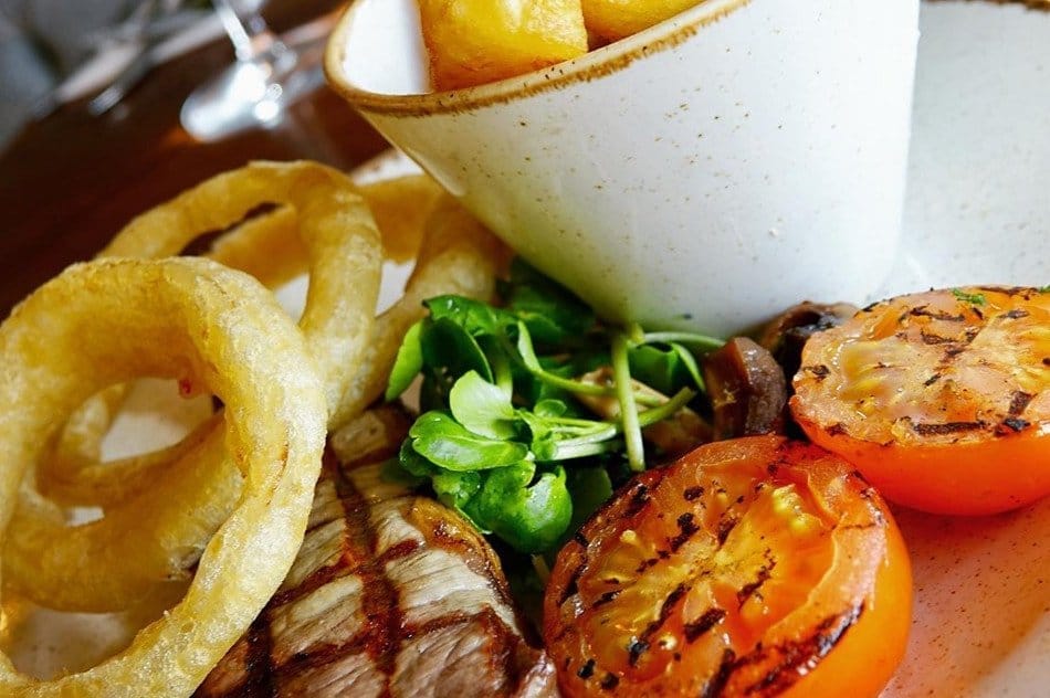 A plate featuring grilled steak, onion rings, and vegetables.