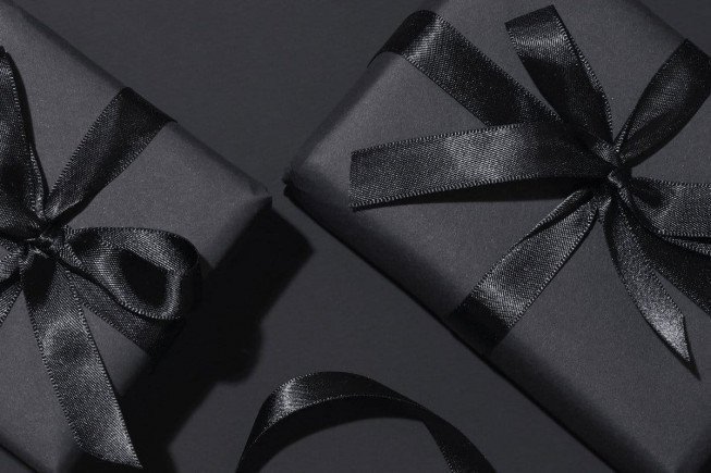 Two black wrapped gifts with satin ribbons on a dark background