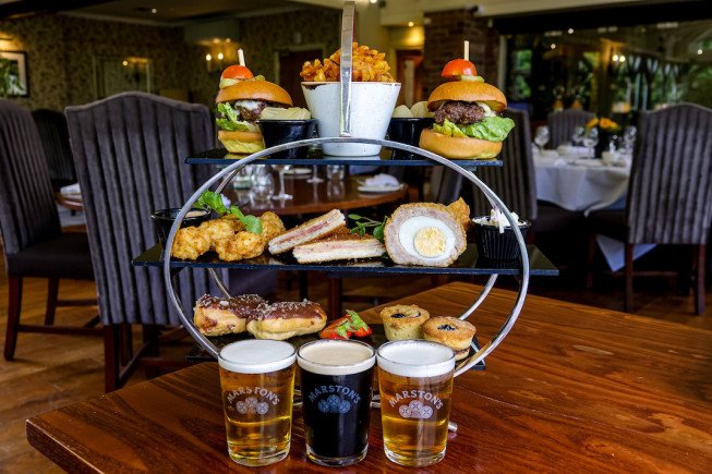 A tiered serving stand with gourmet burgers, snacks, and beer.