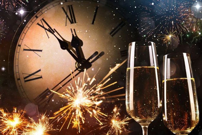 Two champagne glasses with fireworks and a clock in the background